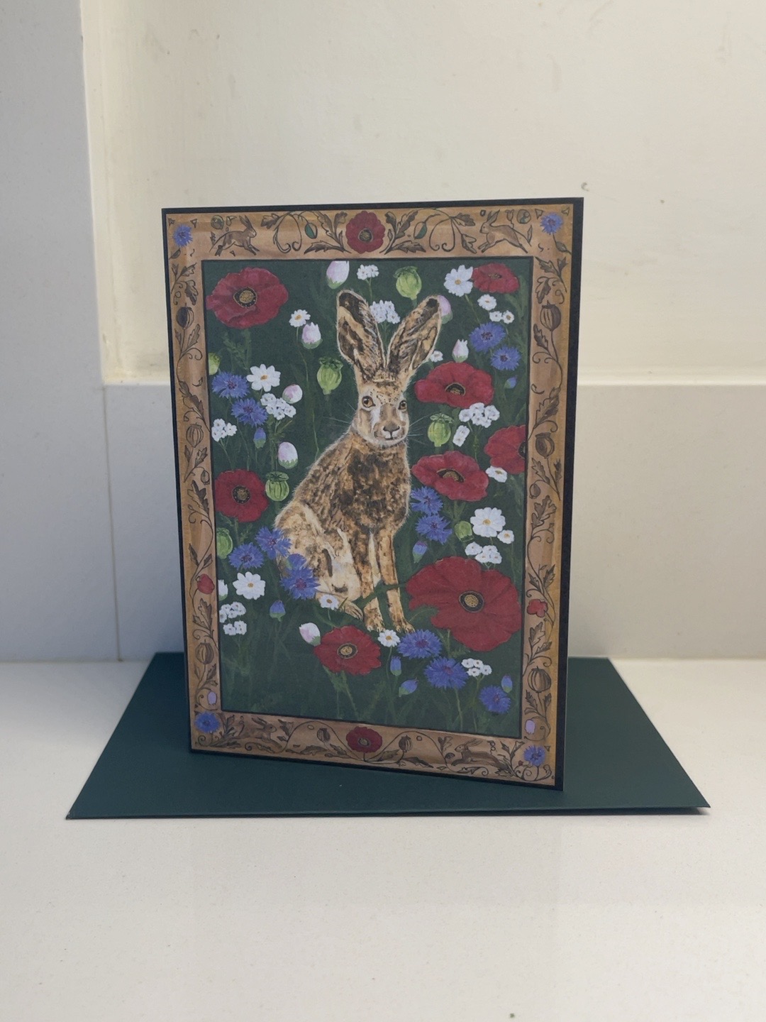 A Fragile Calm hare and flowers art card with its decorative border and dark green envelope